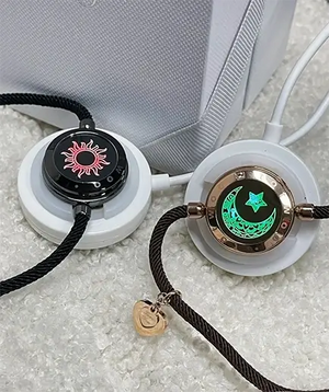 A pair of EntangleTies™ Sun & Moon Totwoo™ Bracelets resting on circular wireless chargers. The bracelets glow in red and green, highlighting the sun and moon designs.